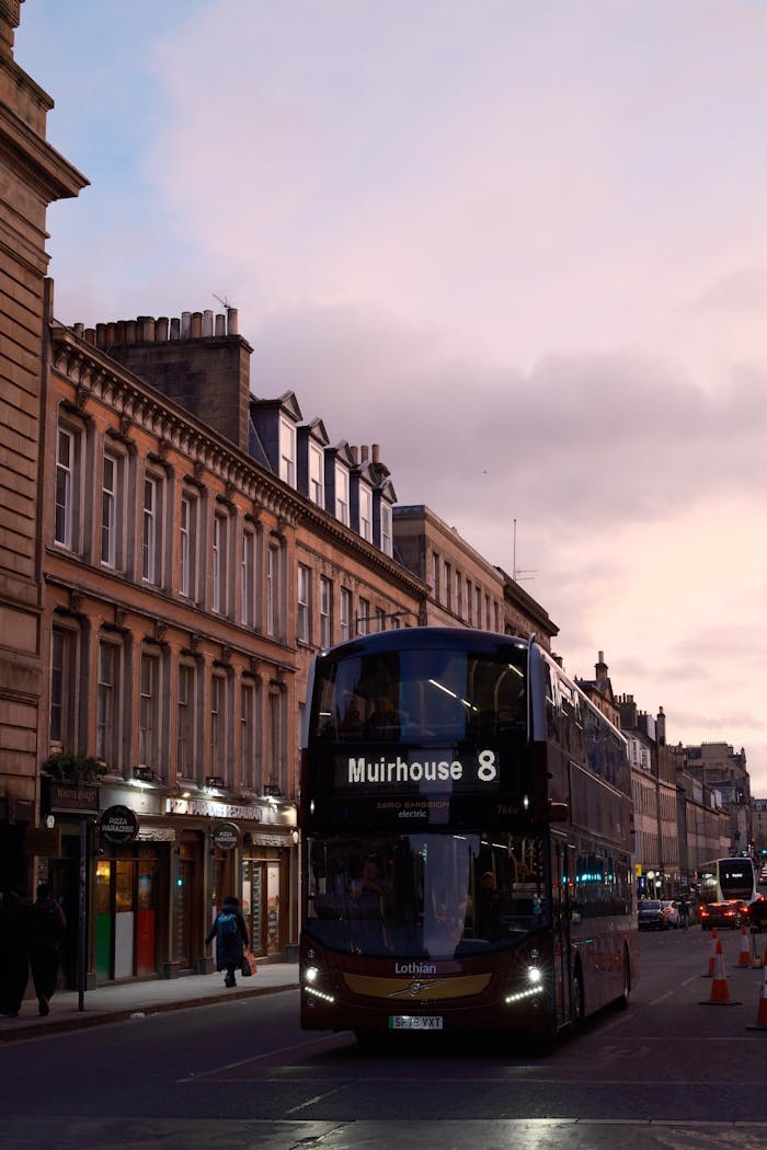 A Lothian double-decker bus on a historic Edinburgh street at twilight.