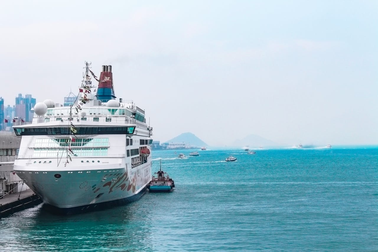 A luxury cruise ship docked at a bustling harbor with clear blue waters and city skyline backdrop.