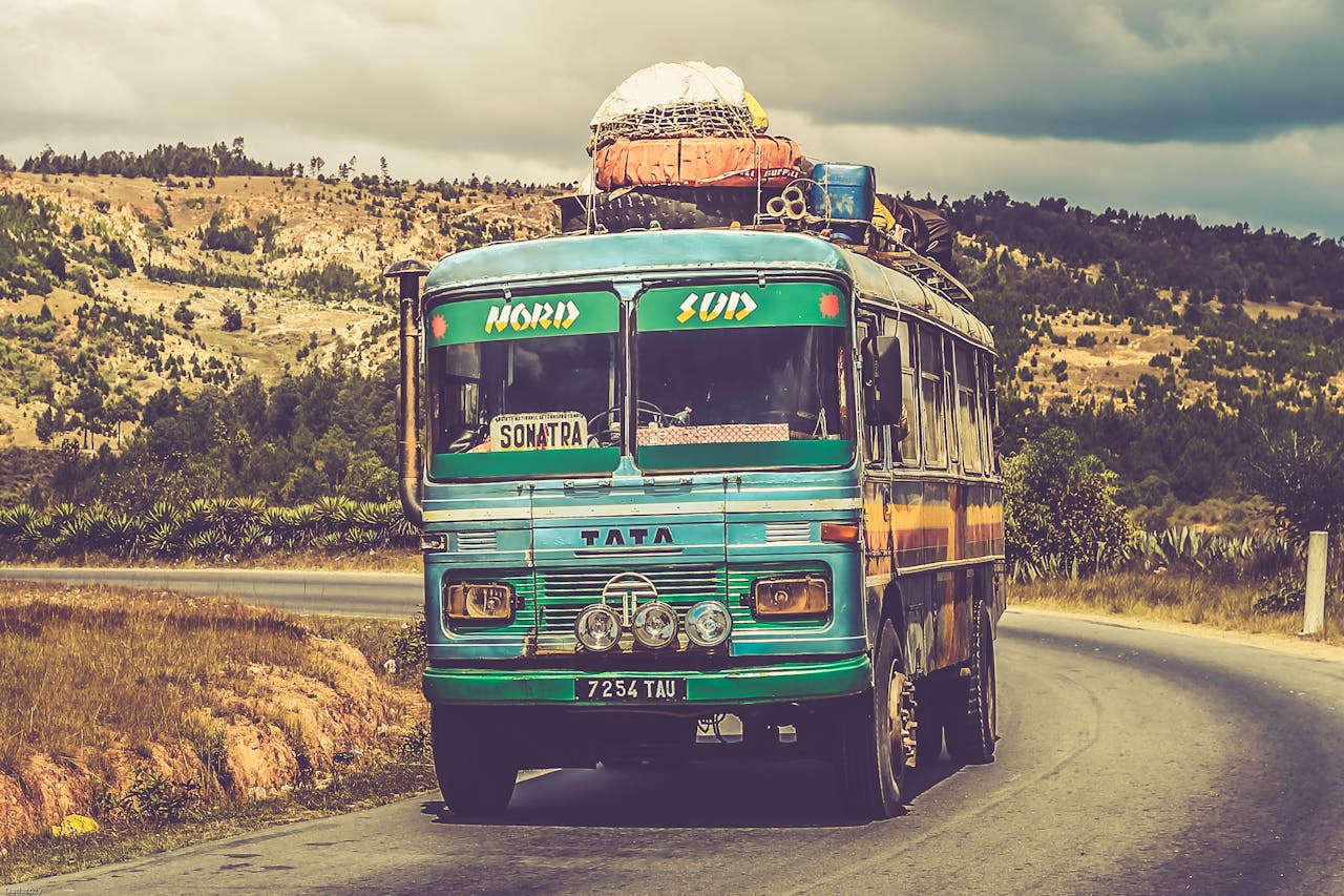 Colorful vintage bus traveling on a scenic countryside road under a cloudy sky.