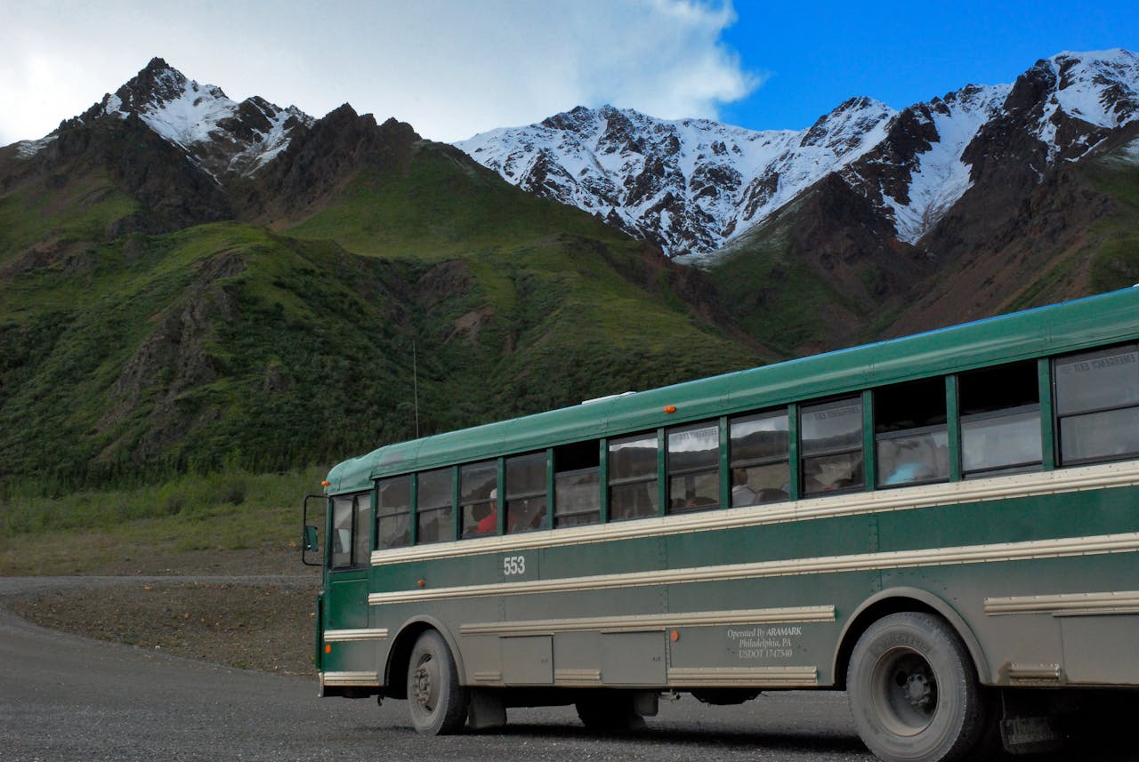 Explore the wilderness with a vintage bus journey through lush mountain landscapes under bright blue skies.